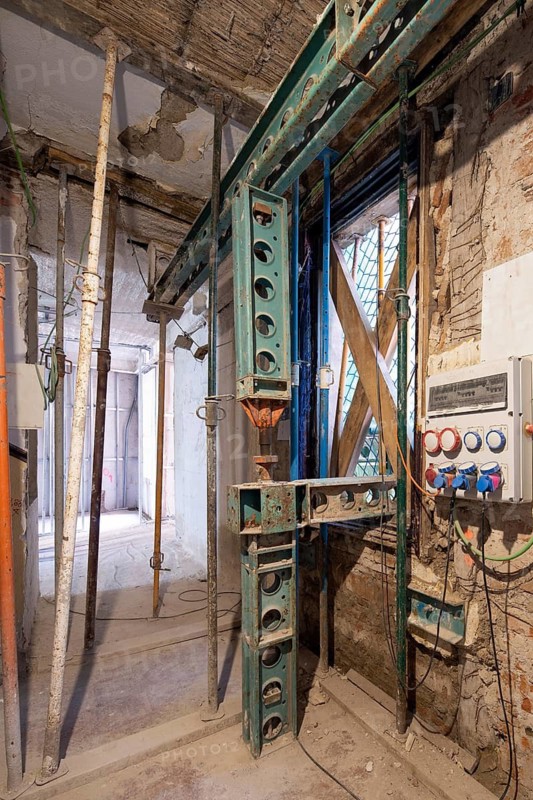 Industrial construction site showing metal support beams, exposed wiring, and a partially built wall. A mix of old and new elements reveals ongoing renovation work