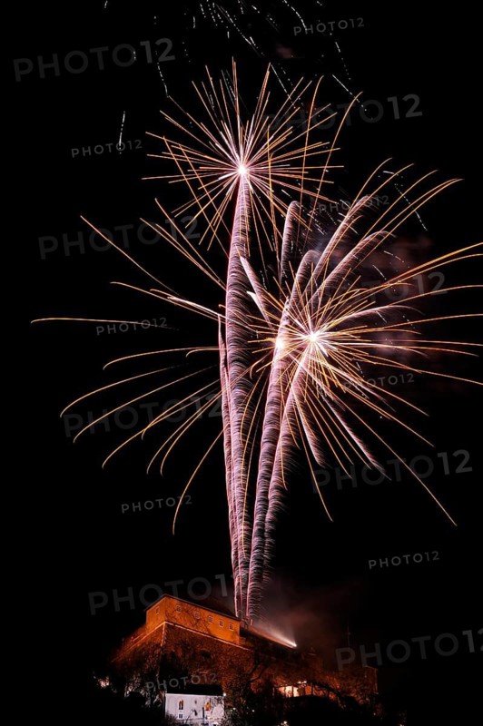 Golden firework tails sparkle majestically in the night over an illuminated building, New Year's Eve, Stallbastei, Schlossberg, Graz, Styria