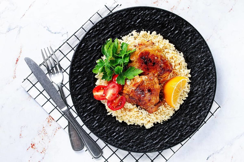 Grilled chicken served with couscous with fresh vegetables and herbs on a black platter, Greek cuisine, homemade