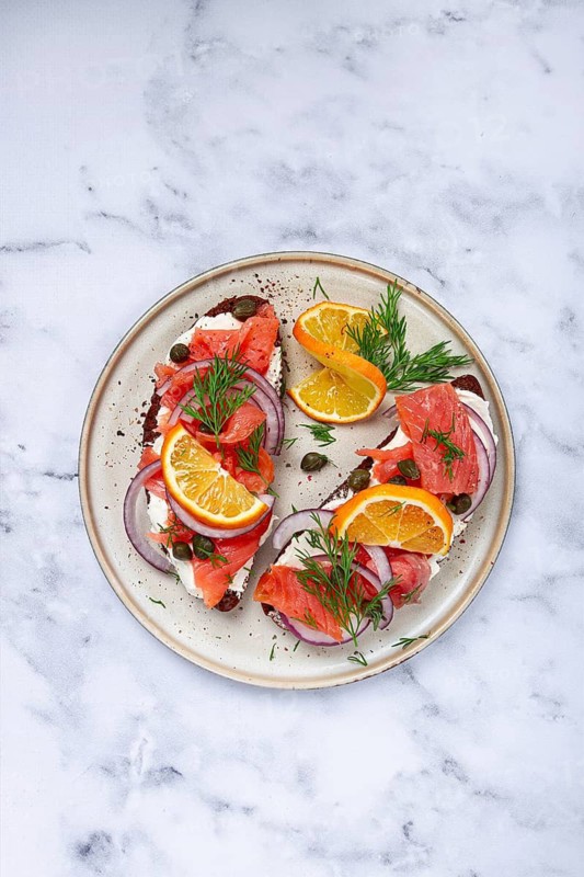 Sandwich with freshly smoked salmon, on black bread, with cottage cheese, with herbs and red onions, capers and pieces of citrus fruits, on a marble countertop, breakfast, no people