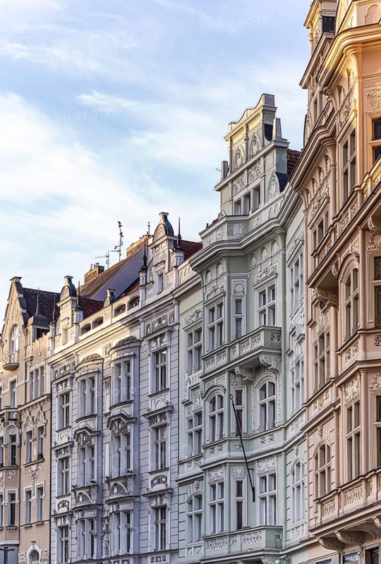A row of ornate historic buildings with intricate facades and pastel hues under a clear evening sky. The soft light enhances the architectural details and vibrant colors of Prague