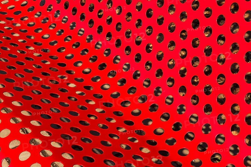 Close-up of vibrant red painted metal sitting bench and backrest with perforated round holes, Quebec, Canada