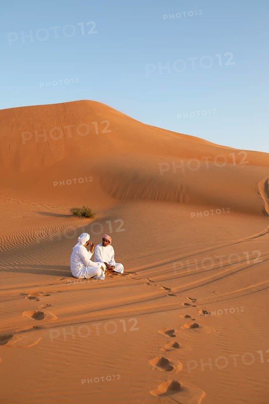 Bedouin men in white dishdashas sitting on a sand dune, Wahiba Sands desert or Rimal Al Wahiba or Sharqiyya Sands, Janub ash-Sharqiyya region, Oman