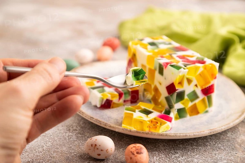 Colored Fruit and milk jelly with hand on brown concrete background and green linen textile, side view, close up, minimalism, selective focus