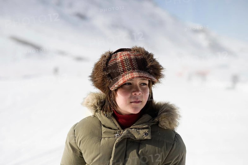 A child stands in a warm jacket and hat, enjoying the snowy landscape of Sierra Nevada Ski Resort in Granada. The winter scene exhibits natural beauty and leisure