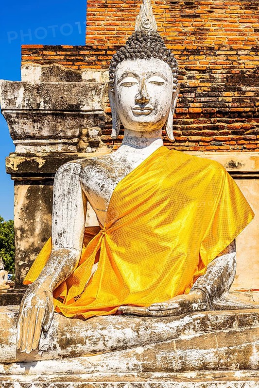 Stone Buddha statue decorated with yellow cloth, historic Buddhist temple complex, Ayutthaya, Thailand