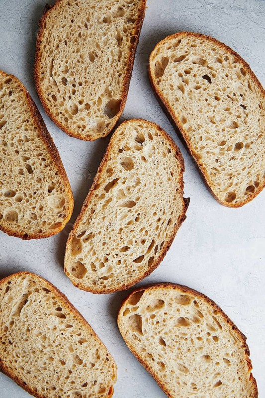 Top view of freshly sliced sourdough bread with a textured, porous interior on a gray background