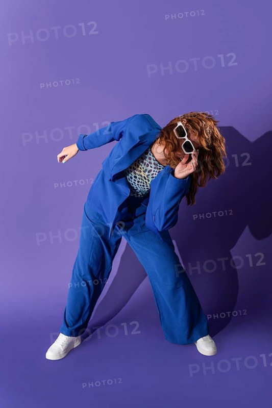A young woman in a vibrant outfit dances energetically against a purple background, exuding joy and grace. Her modern dance pose combines style and passion seamlessly