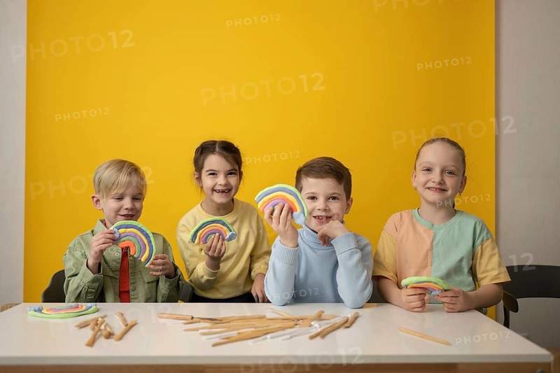 Children enjoying a creative art lesson, crafting colorful modeling clay rainbows. The bright setting, with yellow and pastel tones, highlights fun and imagination