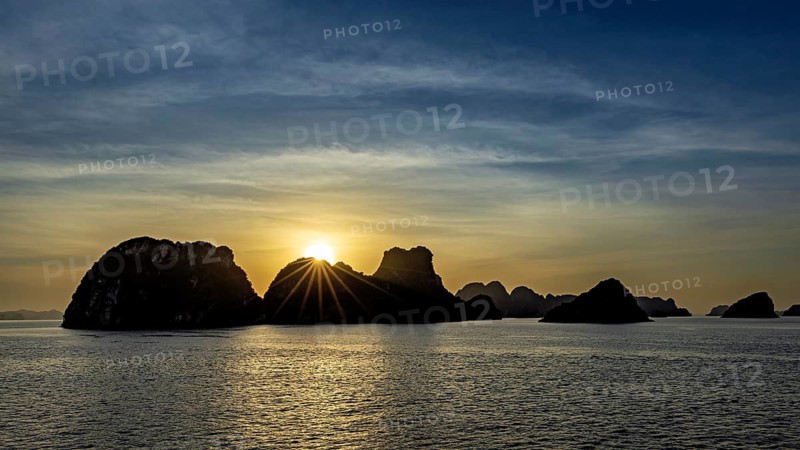 Boats sail past jagged rocks on a calm sea at sunset, sunset in Halong Bay in Vietnam