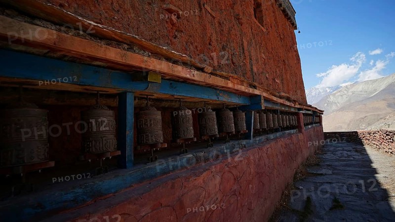 Long row of prayer wheels against a red brick wall under a clear sky, Managn, trekking at Annapurna Circuit, Nepal