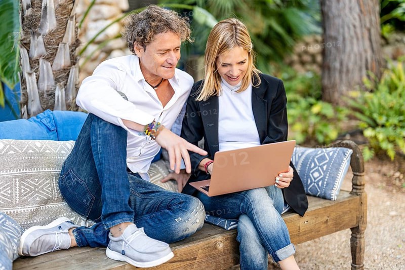 A couple works together on a laptop in their cozy outdoor home office, surrounded by lush greenery They are focused and engaged, enjoying the flexible work-from-home atmosphere