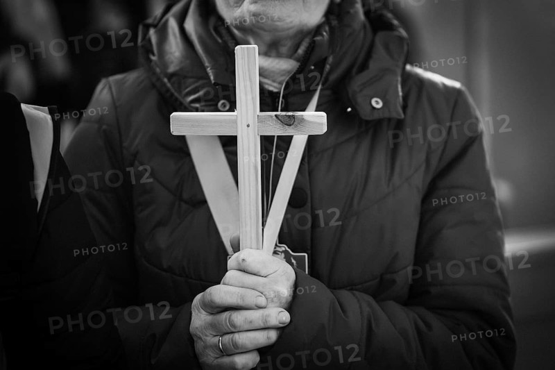 Black and white close-up of hands holding a simple wooden cross during a religious ceremony or prayer in Poland