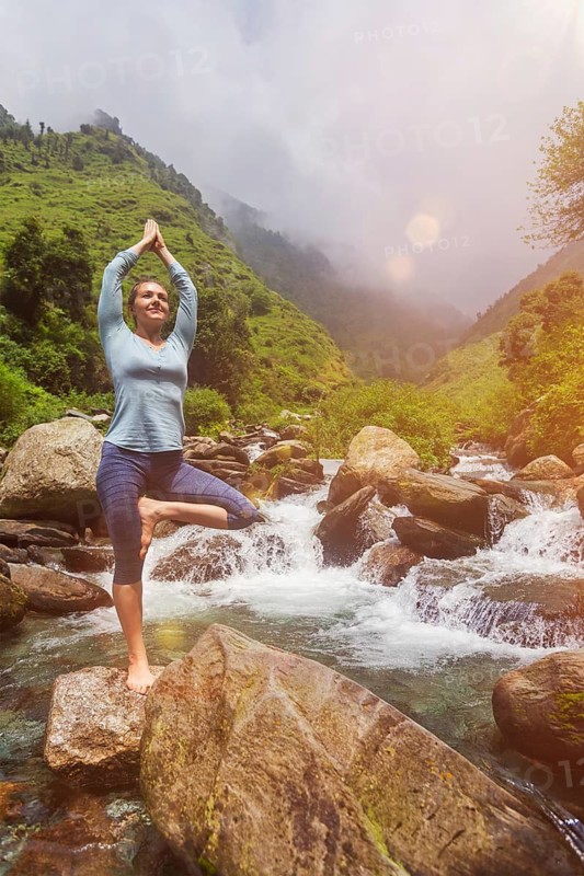 Woman in Hatha yoga balance yoga asana Vrikshasana tree pose at waterfall outdoors