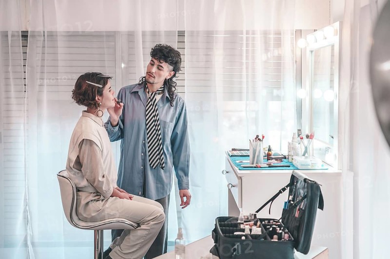 Professional makeup artist applying lipstick on a model in a bright and modern beauty salon, surrounded by makeup tools and equipment, showcasing diversity and inclusion in the beauty industry