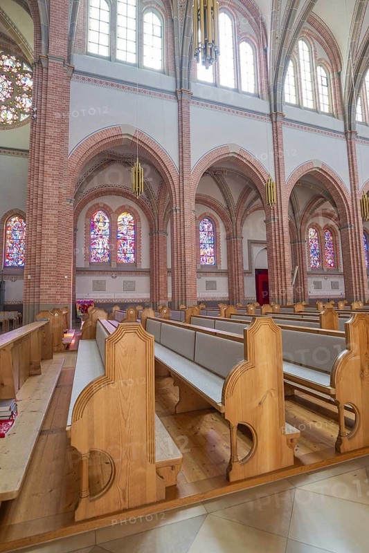Interior of church with light wooden benches and colorful glass windows in Gothic style, Sacred Heart Cherry, Bregenz, Austria