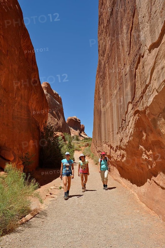 Three hikers walk through a narrow gorge between high sandstone walls, Arches National Park, Utah, USA
