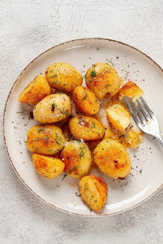 Half-eaten fried new potatoes, with butter and dill, on a white plate, with a fork, at home, no people
