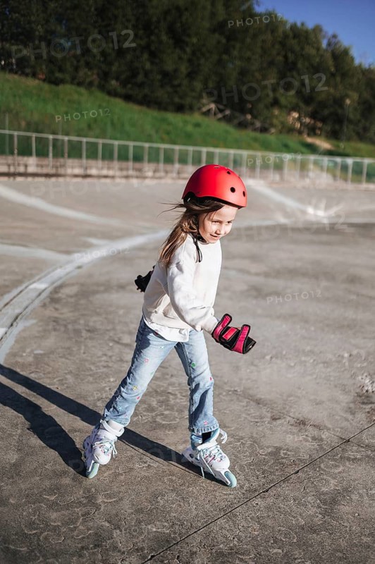 Active young girl roller skating outdoors in a park, wearing helmet and wrist guards for safety