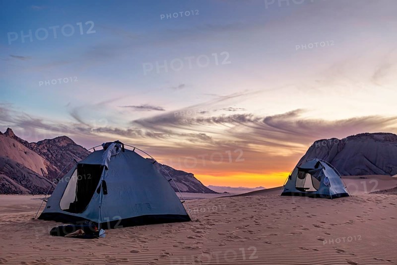 Two tents in a desert at sunset with mountains in the background and a colourful sky, tent camp in the Sahara desert in Algeria