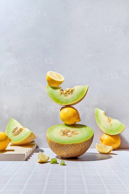 A dynamic arrangement of melons and lemons on a tiled surface. The summer vibes are highlighted by hard lighting and contrasting vibrant colors, creating a refreshing visual