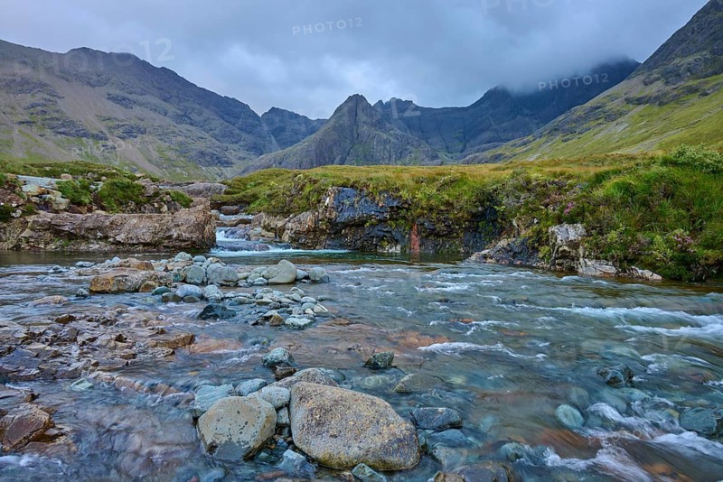 A clear river flows through a rocky landscape surrounded by high mountains under a cloudy sky, Fairy Pools, Grula, Isle of Skye, Scotland, United Kingdom, Great Britain