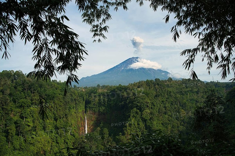 This picturesque landscape captures Kaspa Biru Waterfall majestic peak shrouded in clouds, accompanied by a cascading waterfall amidst a dense tropical forest