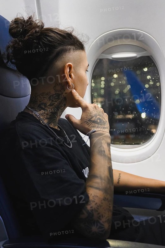 A young woman with elaborate tattoos looks through an airplane window, admiring the lights The nighttime scene offers a sense of wonder and introspection