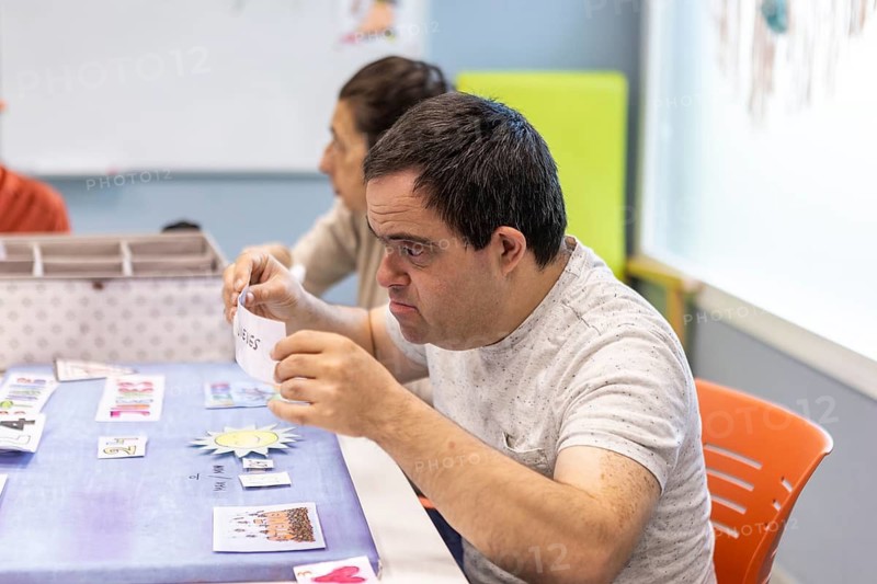 A person with a mental disability engages in a structured activity at a day center, illustrating support, learning, and care in a nurturing environment