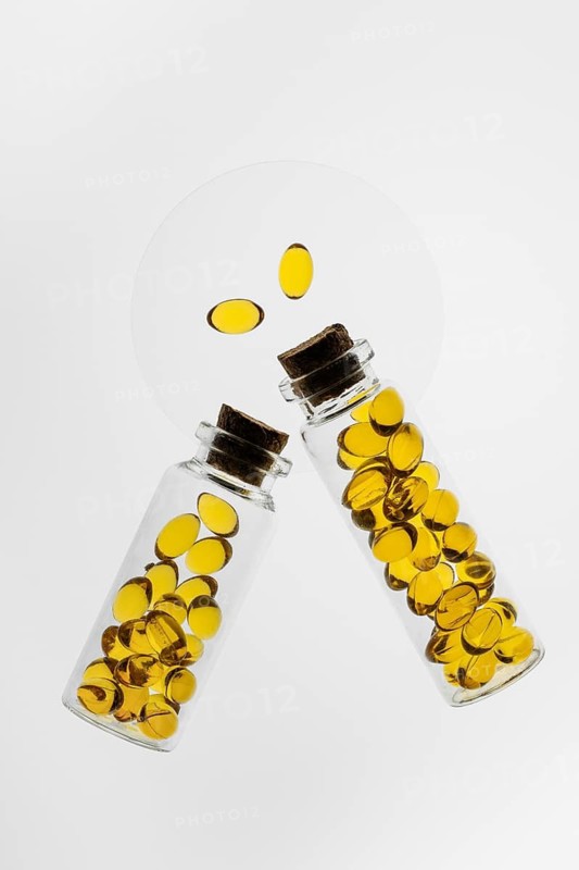 Two transparent glass bottles filled with yellow Omega-3 and Vitamin D capsules on a white background, emphasizing health and nutrition