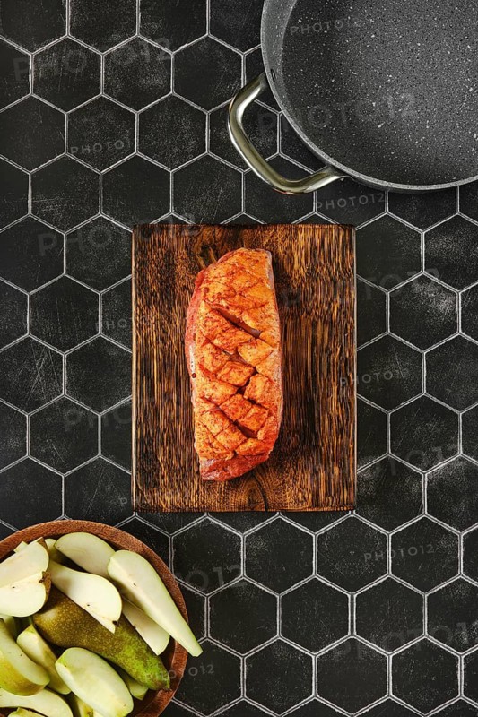 Top view of a juicy marinated spice rubbed duck breast on a wooden chopping board beside fresh vegetables and baking pan