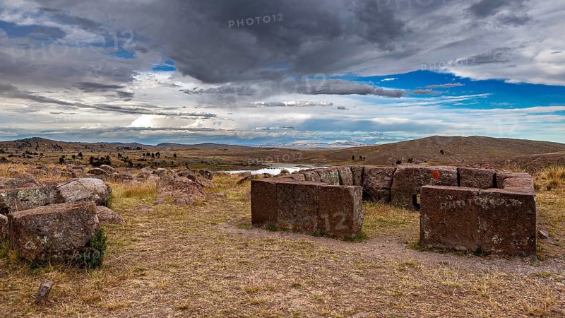 Round stone structures under a dramatic sky in a wide landscape, The Chullpas of Sillustani near Puno in Peru