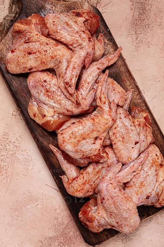 Chicken wings, marinated and laid out on a wooden platter, ready for cooking, grilling or baking, in a home kitchen, there are no people