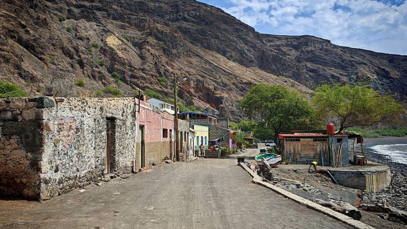 Main street and town view with buildings and fishing boat in front of a hut, rural road along a coastal rock face, beach and sea on the right, hiking, Tarrafal de Monte Trigo, Santo Antao, Cabo Verde, Cape Verde, Cape Verde