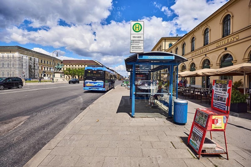Odeonsplatz bus stop, bus stop sign, bus shelters, public transport, public transport, public trash can, press box, general architecture, houses, road made of asphalt, footpath made of sidewalk tiles, blue sky, cumulus clouds, Odeonsplatz, Ludwigstraße, Munich, state capital, district-free city, Bavaria, Germany
