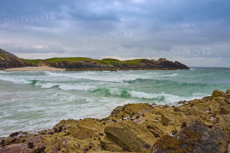 A wild coastline with breaking waves rolling across the rocks under a gloomy sky, Clachtoll Beach, Clachtoll, Lairg, Scotland, United Kingdom, Great Britain