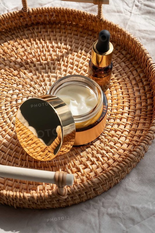 A luxurious skincare set featuring a cosmetic of cream and a dropper bottle on a woven basket. The golden accents and natural texture exude elegance and sophistication