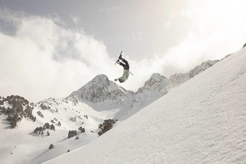 A snowboarder skillfully performs a thrilling freeride trick on a snowy mountain slope, surrounded by stunning, rugged peaks under a clear sky, capturing the spirit of winter adventure