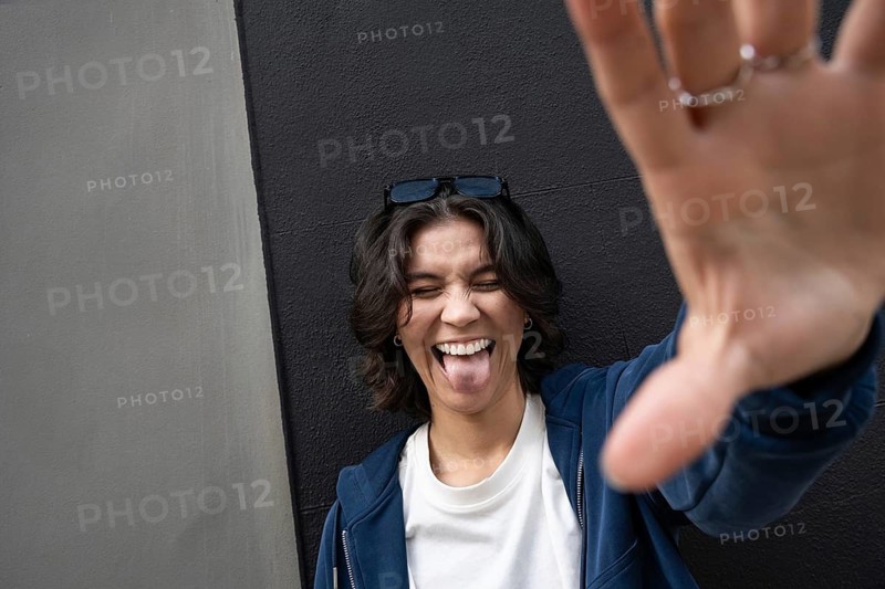 A person playfully sticks out their tongue and smiles broadly, wearing casual attire. Sunglasses rest on their head, adding to the relaxed, fun vibe of the image