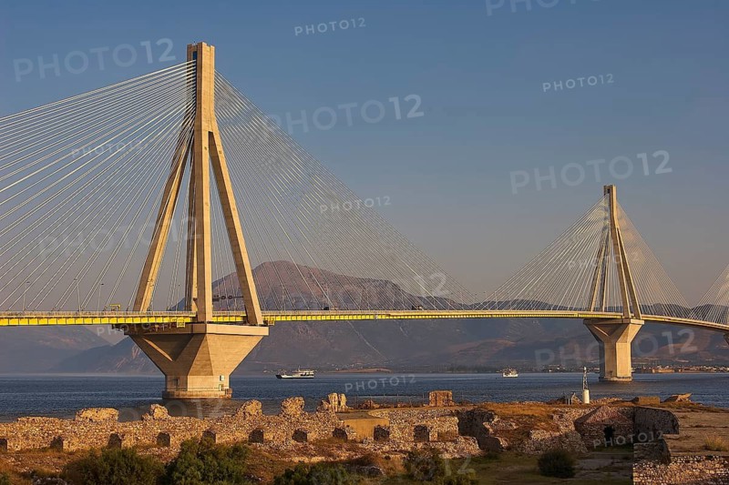 A long modern bridge stretches across the sea surrounded by ruins and mountains in the background, Rio-Antirrio cable car bridge, Rio fortress, Patras, Peloponnese, Greece