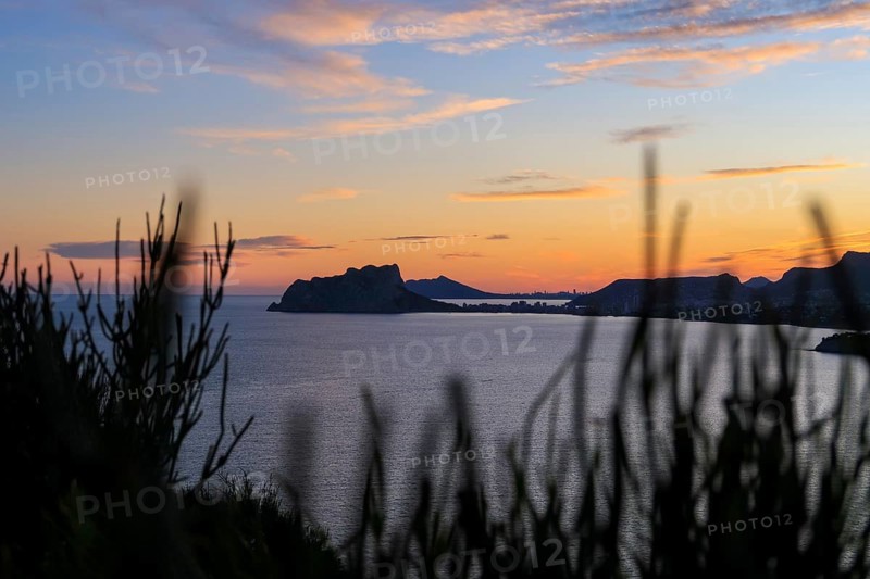 Captivating view of a Costa Blanca sunset over the Mediterranean Sea, with a serene seascape framed by silhouetted foliage and a colorful sky