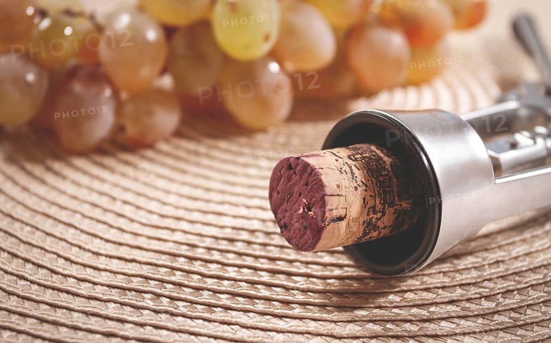 A corkscrew with a wine bottle stopper, lying on a woven napkin, with green grapes