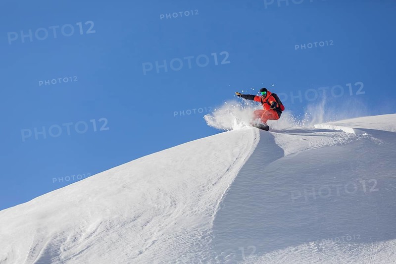 A snowboarder in bright gear carves down a pristine, snow covered slope, sending up a spray of snow under a clear blue sky, showcasing the thrill of winter sports