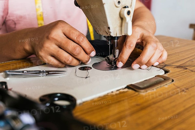 Hands of a asian seamstress using a vintage sewing machine to stitch fabric. The wooden table holds scissors and threads, illustrating traditional craftsmanship in a workshop setting