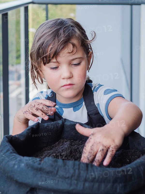 Young girl focused as he handles soil in black fabric pot, possibly preparing for planting sunflowers