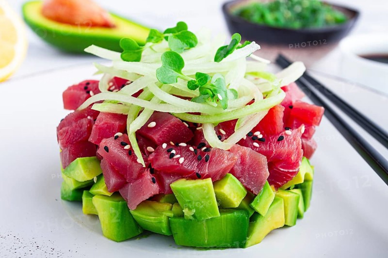 Fresh tuna tartare with avocado served on a marble table with soy sauce and seaweed salad