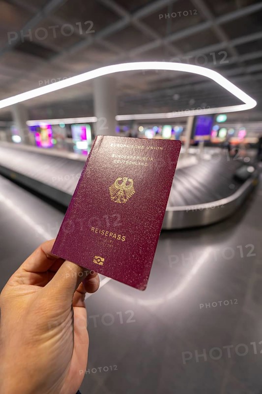 12.03.2026 hand holding German passport with baggage carousel in background at airport terminal, travel context at Frankfurt Airport, Hesse, Germany