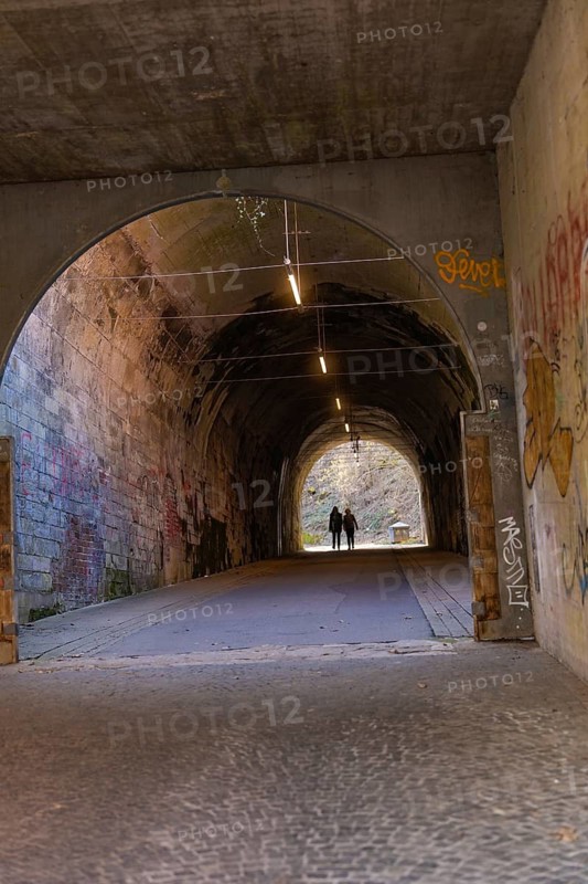 Concrete tunnel with graffiti and two people in the background, illuminated by interior light, Schwäbisch Hall, Germany
