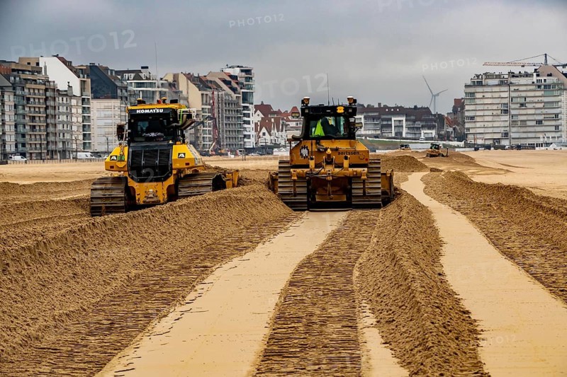 Bulldozers when distributing sand on the beach in the town of Knokke-Heist, part of coastal protection and beach maintenance, due to floods, erosion and sea level rise, the sand on the beach is repeatedly washed into the sea, in winter the sand from the seabed is washed back onto the beach with suction vessels, the excavators and levelers then distribute the sand back on the beach to eliminate the difference in height so as to bathe To make the beach usable again for the next season