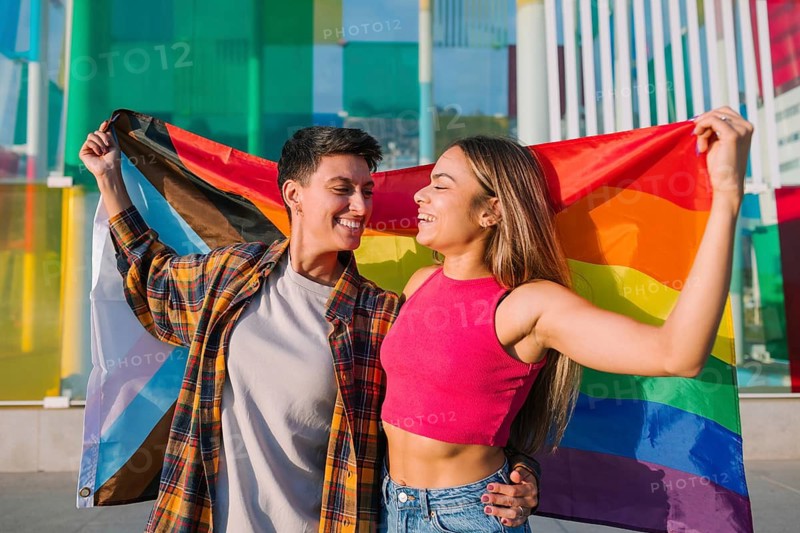 A joyful lesbian couple celebrates love and diversity, waving a Pride and Transgender flag outdoors. This image highlights LGBTQIA+ pride, equality, and an inclusive relationship